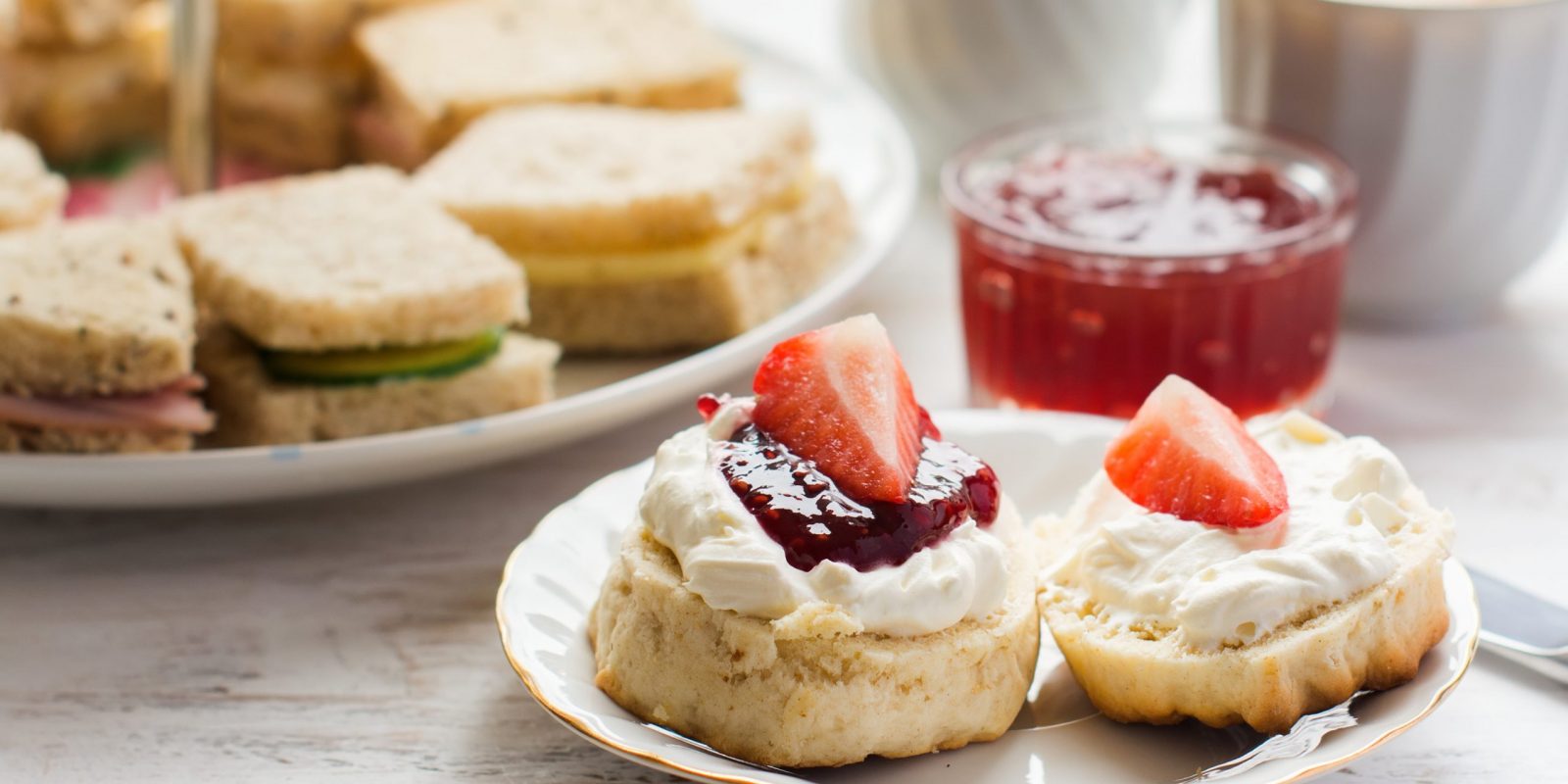 Traditional English afternoon tea: scones with clotted cream and jam, strawberries, with various sadwiches on the background, selective focus